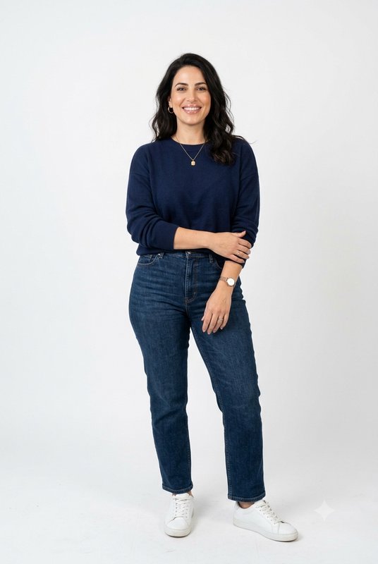 Smiling woman in a casual navy sweater and jeans stands against a plain white studio backdrop