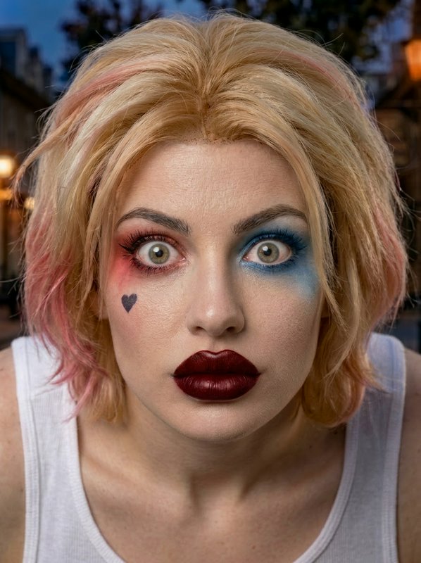 Close-up portrait of a Harley Quinn cosplayer with mismatched makeup and pink-tipped blonde wig s...