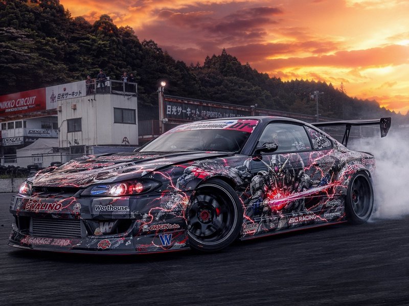 Customized Japanese drift car with a neon lightning wrap performing burnout at a sunset race track.