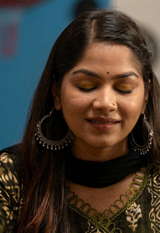 Close-up portrait of a soft-smiling South Asian woman with closed eyes, wearing traditional silve...