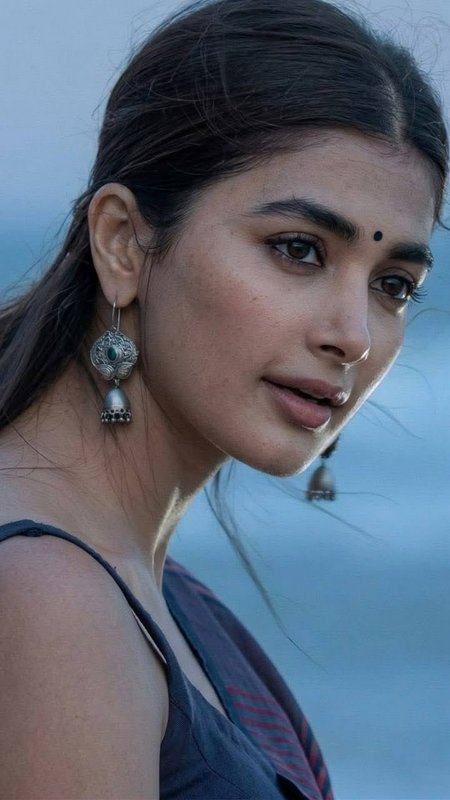 Close-up portrait of Pooja Hegde wearing traditional silver jhumka earrings and a bindi against a...