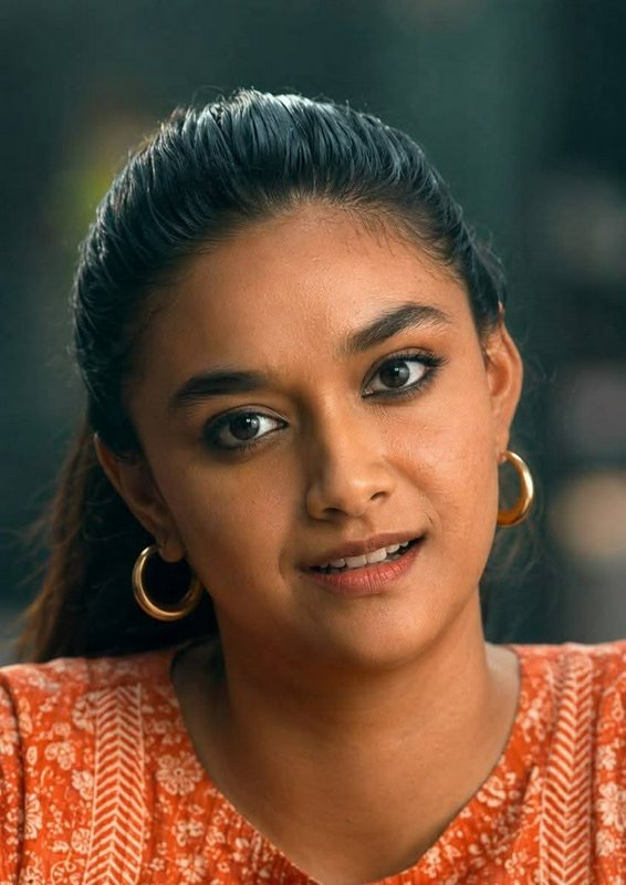Close-up portrait of actress Keerthy Suresh wearing gold hoop earrings and an orange printed top,...
