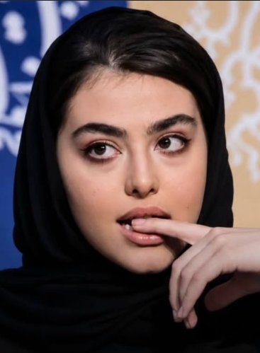 Close-up candid portrait of a young woman in a black hijab, thoughtful expression, finger resting on her lip, looking side...