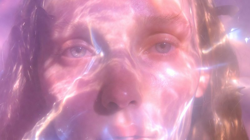 Close-up of a person’s face pressed against translucent pink plastic wrap with soft, reflective l...