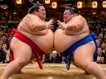 Two sumo wrestlers collide chest to chest mid-bout in a packed traditional sumo arena
