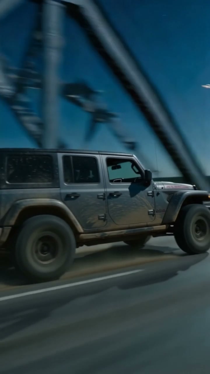 Motion blurred shot of a muddy gray 4-door Jeep Wrangler driving across a steel arch bridge under...