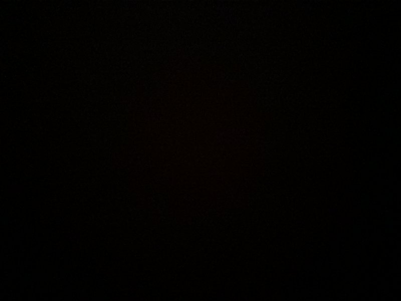 A near-black image with a faint reddish glow at the center.
