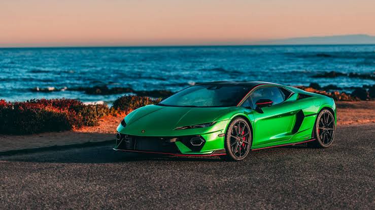 Glossy bright green Lamborghini supercar parked on a coastal road overlooking the ocean at warm g...