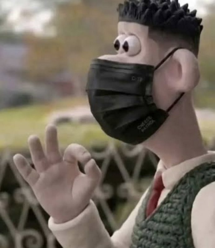 Close-up of stop motion clay character in black face mask making the OK hand gesture against a bl...