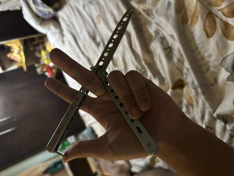Close-up of a hand holding an open perforated stainless steel balisong butterfly knife across out...