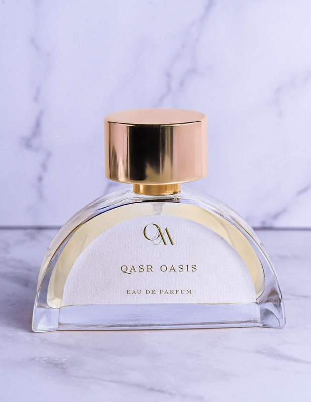 Curved glass Qasr Oasis Eau de Parfum bottle with rose gold cap resting on white marble surface