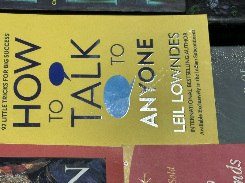 Rotated close-up of the yellow cover of Leil Lowndes' "How to Talk to Anyone" self-help book stac...