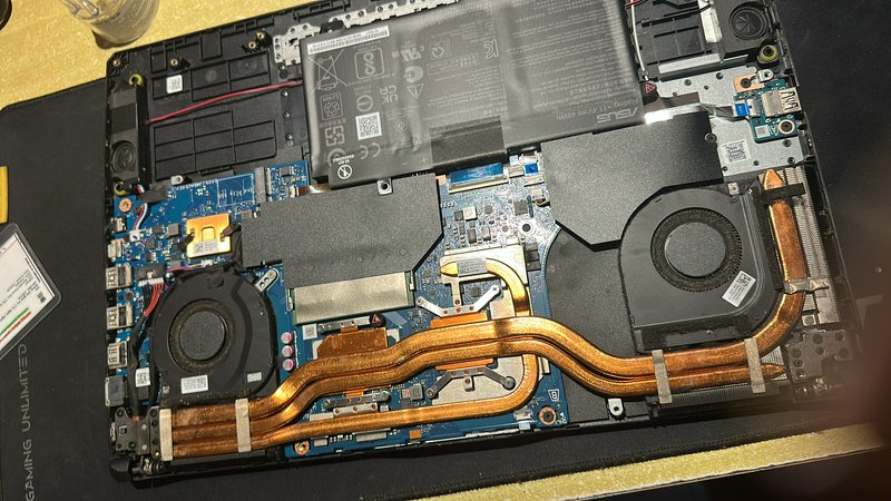 Top-down view of disassembled Asus gaming laptop showing internal motherboard, dual fans, copper ...