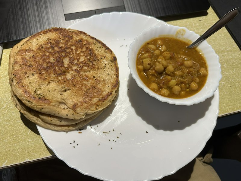 Stack of herb-toasted flatbreads served alongside a bowl of spiced chole chickpea curry on a whit...