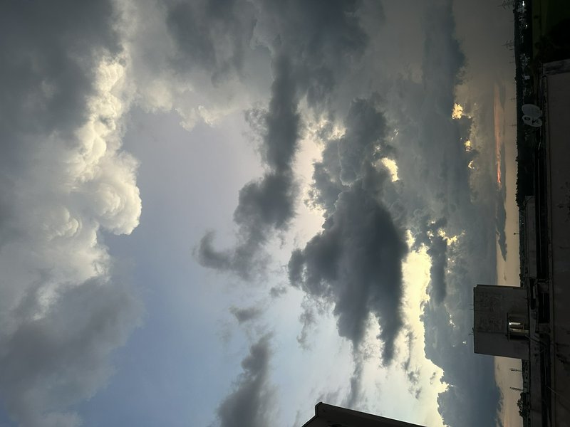 Dramatic sunset sky with billowing backlit storm clouds, viewed from a city rooftop, warm glow il...