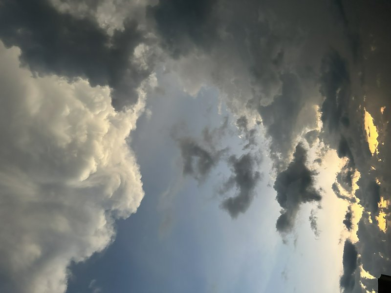 Dramatic towering cumulus storm clouds edged with golden sunset light frame a patch of pale blue sky