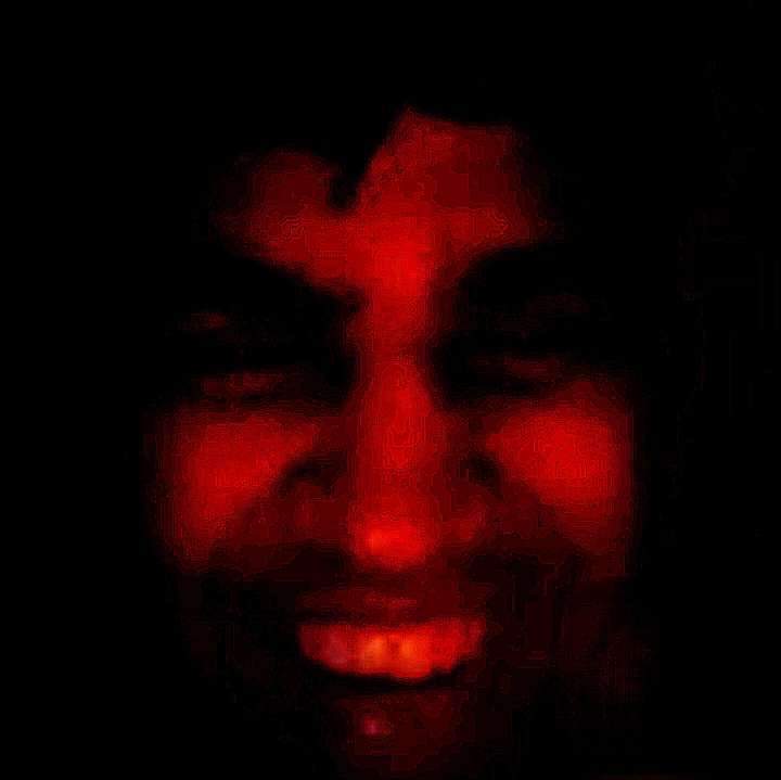 Menacing glowing red grinning face emerging from pitch black darkness