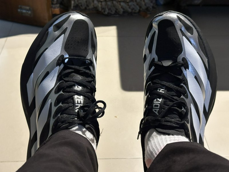 Top-down first person view of black and silver Adidas Adizero running shoes worn on feet indoors