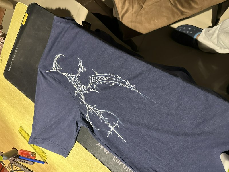 Hand drawn white spiky fantasy dragon design on a navy blue t-shirt laid on a work desk