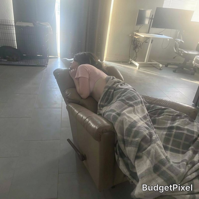 Woman resting face down on a brown leather recliner, covered in a plaid blanket in a sunlit resid...