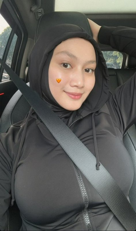 Candid selfie of smiling hijabi woman in black hooded modest activewear, seated buckled in a car ...
