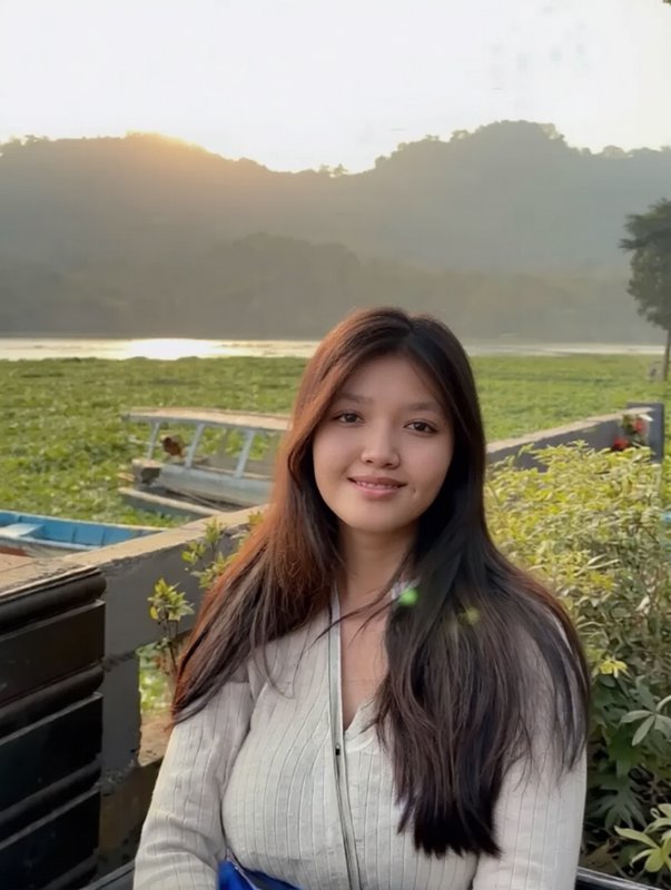 Smiling young woman with long dark hair posing at golden hour overlooking a river and forested hills