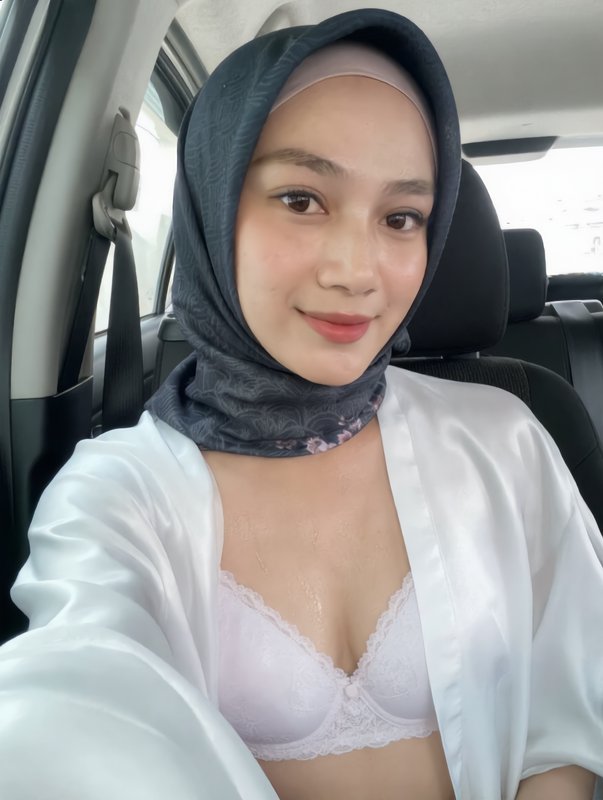 Candid selfie of a smiling young hijabi woman seated inside a car, wearing a dark patterned hijab...