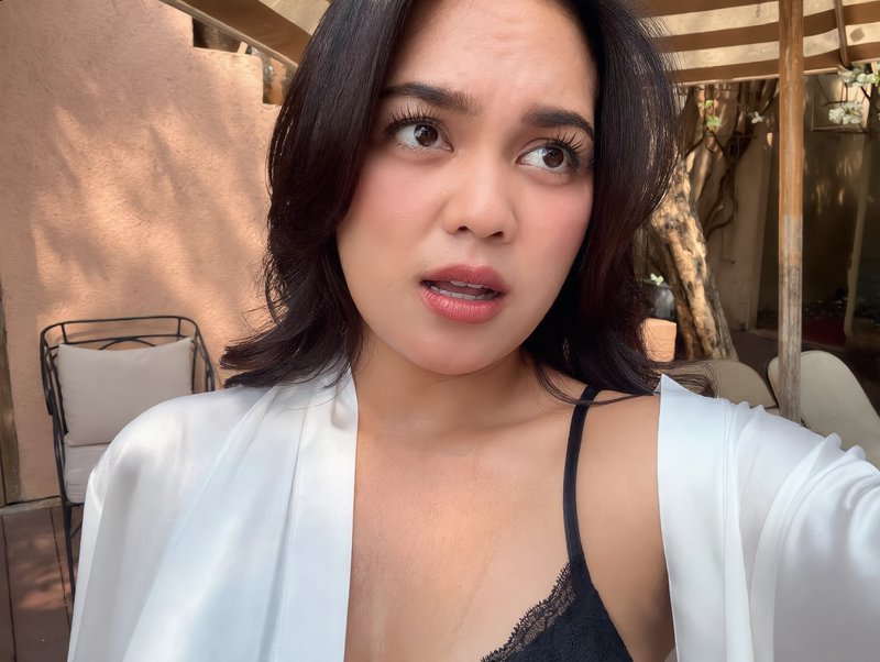 Candid selfie of a surprised young Southeast Asian woman on a sunlit outdoor patio