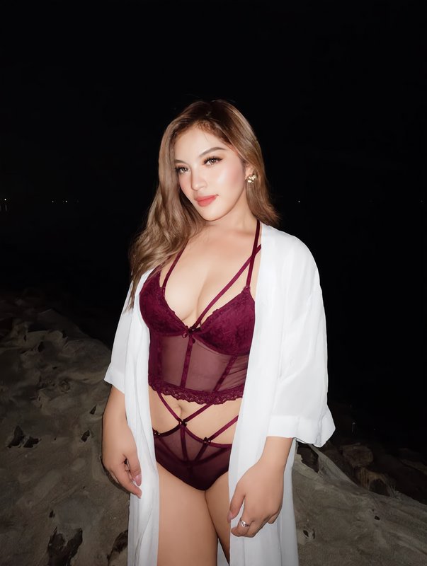 Woman in burgundy lace lingerie and white robe poses on a sandy beach at night