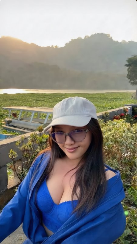 Smiling woman in a white baseball cap takes a selfie overlooking a misty lakeside at golden sunrise