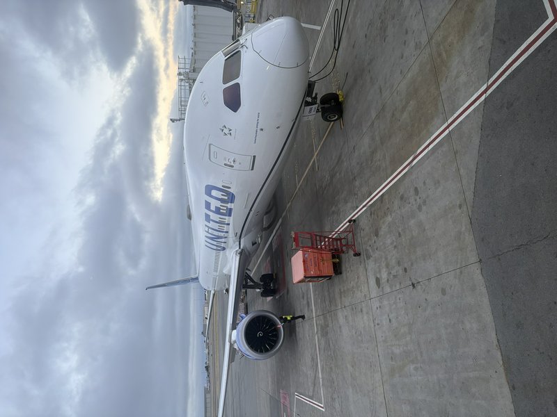United Airlines commercial jet parked on concrete airport tarmac next to ground support equipment...
