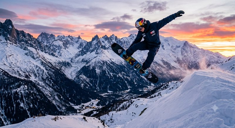 Professional snowboarder mid-air performing a jump trick above snow-covered alpine peaks at color...