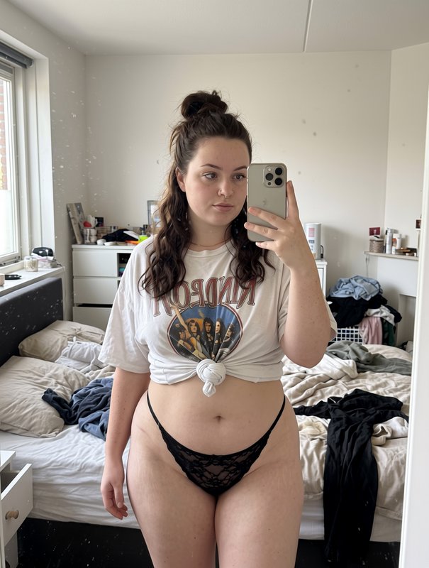 Young woman takes casual mirror selfie in a sunlit lived-in bedroom wearing a knotted vintage ban...