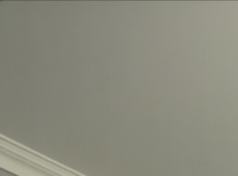 Close-up of smooth matte greige interior ceiling with layered white crown molding trim along the bottom left edge