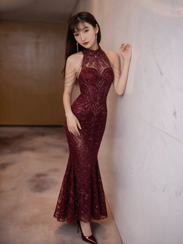 Elegant young East Asian woman in a beaded burgundy mermaid evening gown leaning against a hallwa...