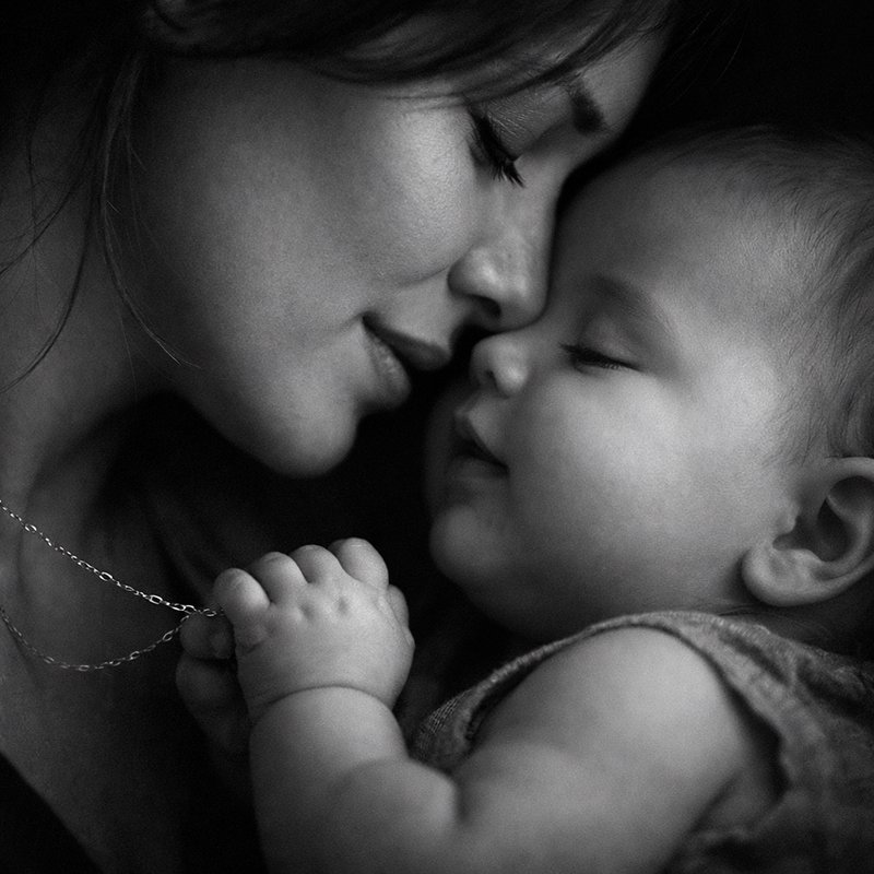 Close-up black and white portrait of a mother tenderly nuzzling her sleeping infant