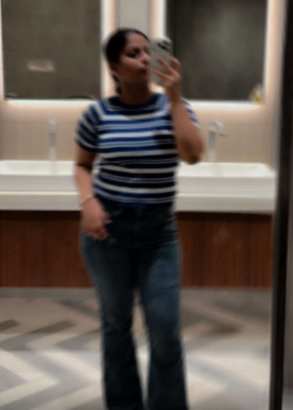 Blurred candid mirror selfie of a woman in a striped top and flared jeans taking a photo in a mod...