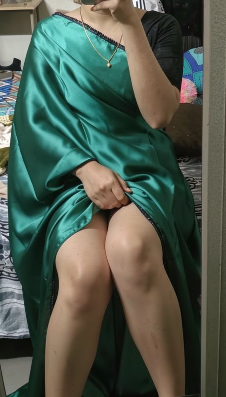 Mirror selfie of a seated woman wearing a glossy emerald green satin saree with black trim, in a ...