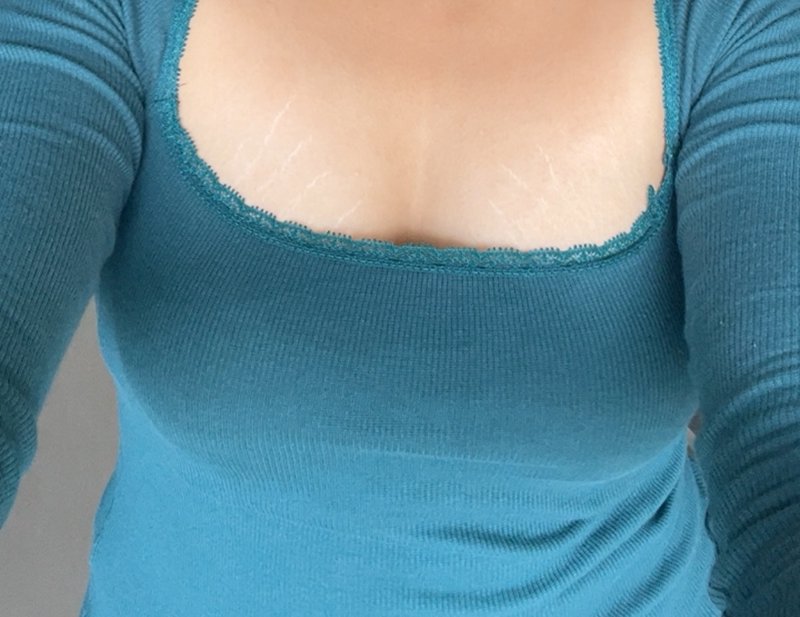 Close-up view of a teal ribbed long sleeve top with delicate lace trim on its square neckline, wo...