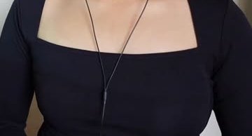 Close-up of a person wearing a fitted black square neck top with thin wired earbud cords across t...