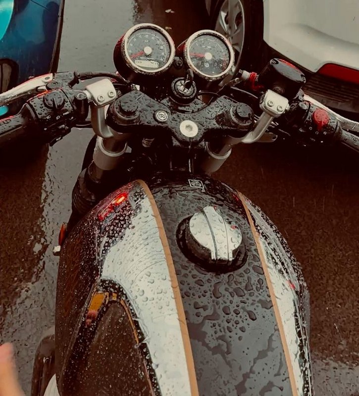 First person view of a rain-soaked Royal Enfield motorcycle, showing its striped fuel tank and du...