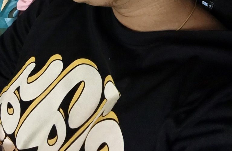 Close-up of a person wearing a black crewneck graphic t-shirt with white and gold bubble letter p...