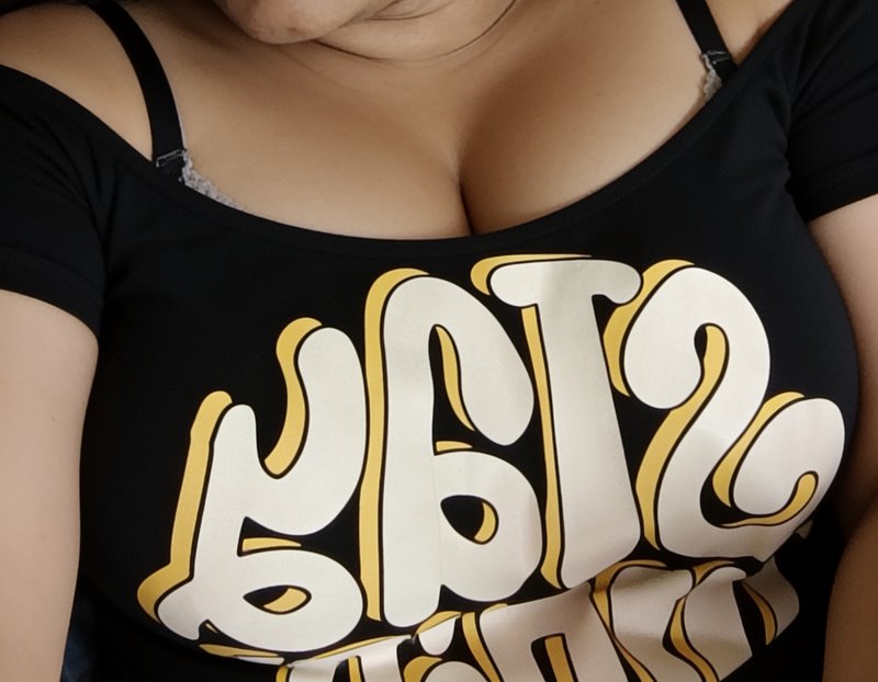 Close-up of a person in a black off-shoulder graphic tee with reversed retro bubble text, bra str...