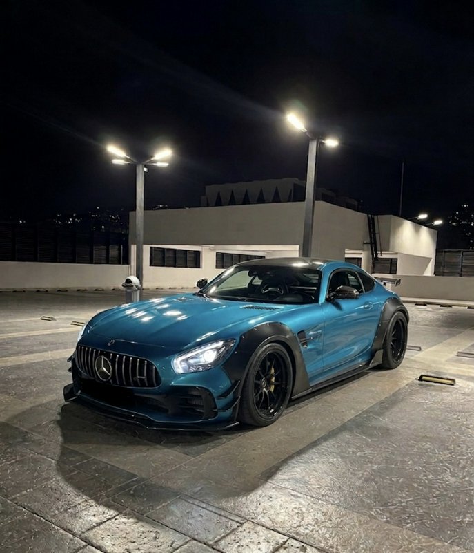Custom widebody teal Mercedes AMG GT sports car parked on a lit rooftop parking lot at night