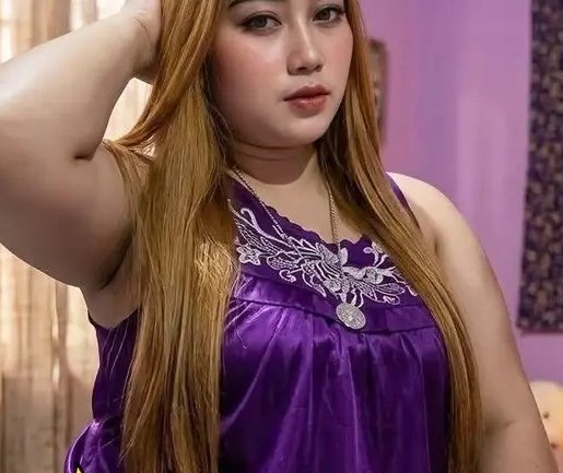 Close-up portrait of a woman with long golden hair wearing an embroidered purple satin top, hand raised behind her head.