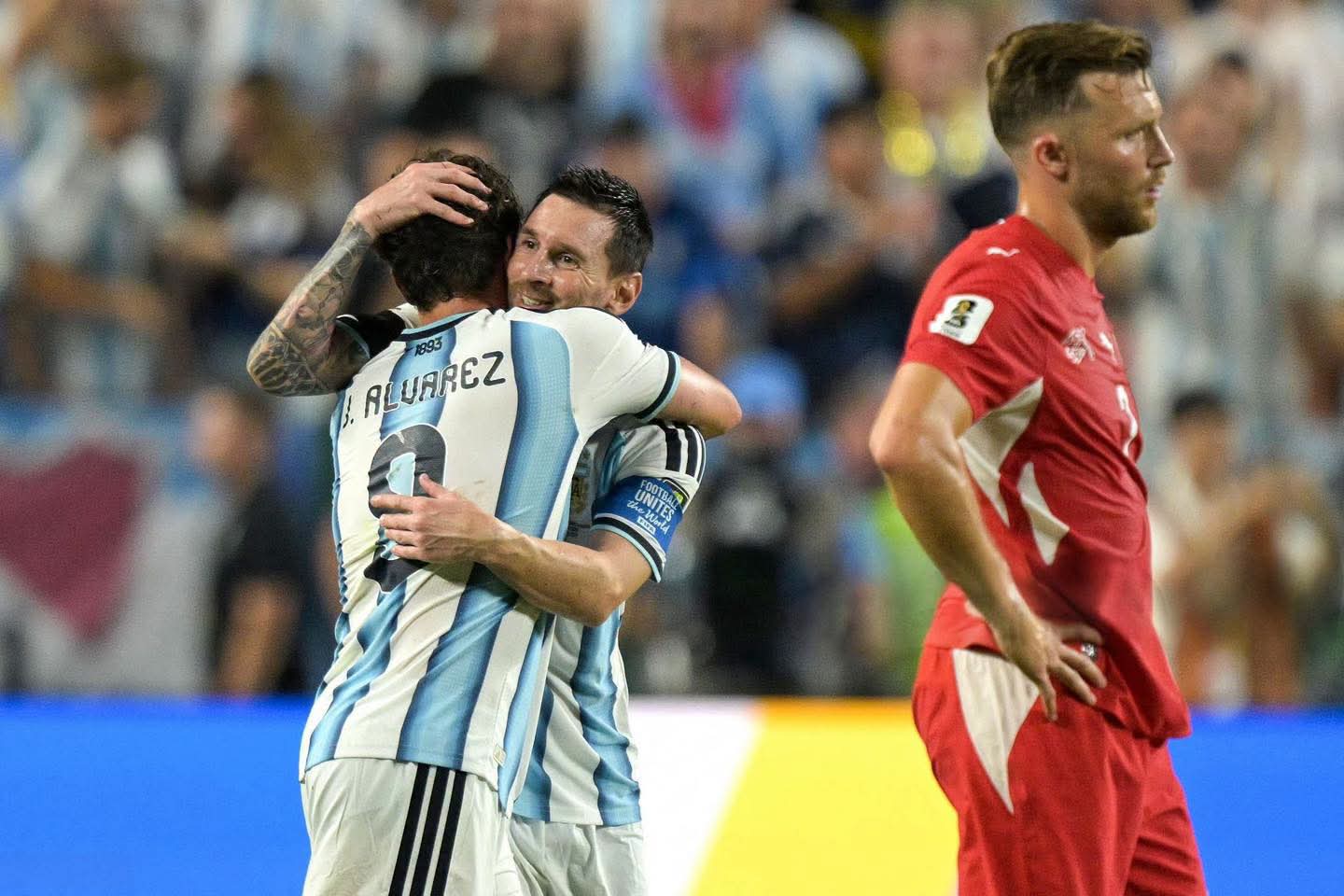 [Lionel Messi hugs teammate Julian Alvarez in Argentina kits, an opposing red-uniformed player stands nearby on a World Cu...