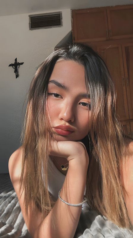 Sunlit casual selfie of a young woman with ombre hair resting her chin on her hand in a cozy bedroom