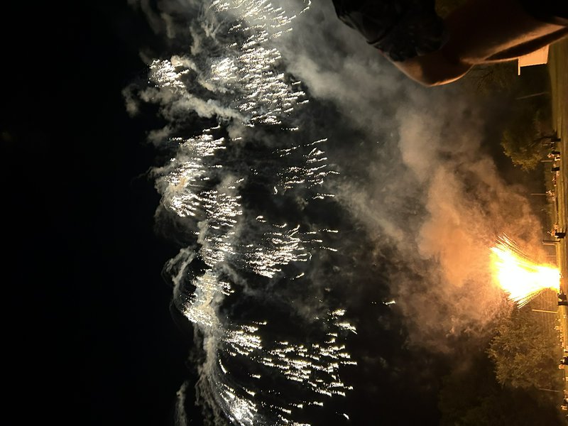 Golden fountain fireworks erupt against a dark night sky, wispy smoke drifting, shot from an outdoor evening celebration.