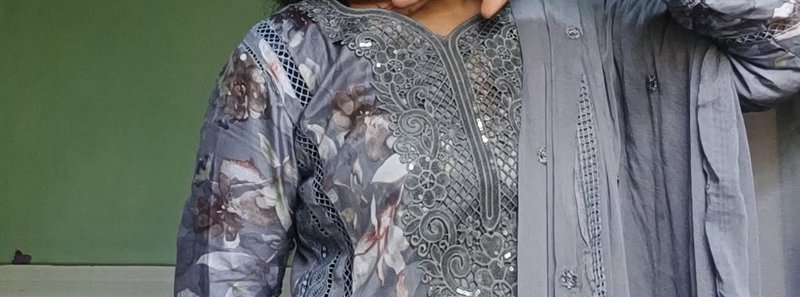 Close-up view of a grey embroidered floral salwar kameez with cutwork lace details against a sage...