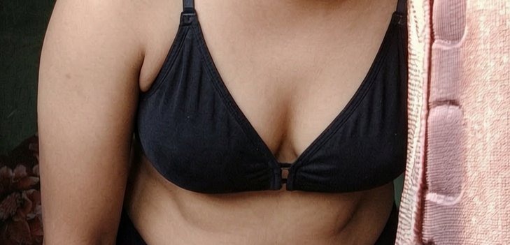 Close-up of a person wearing a black front-clasp wireless triangle bra, framed with soft pink tex...